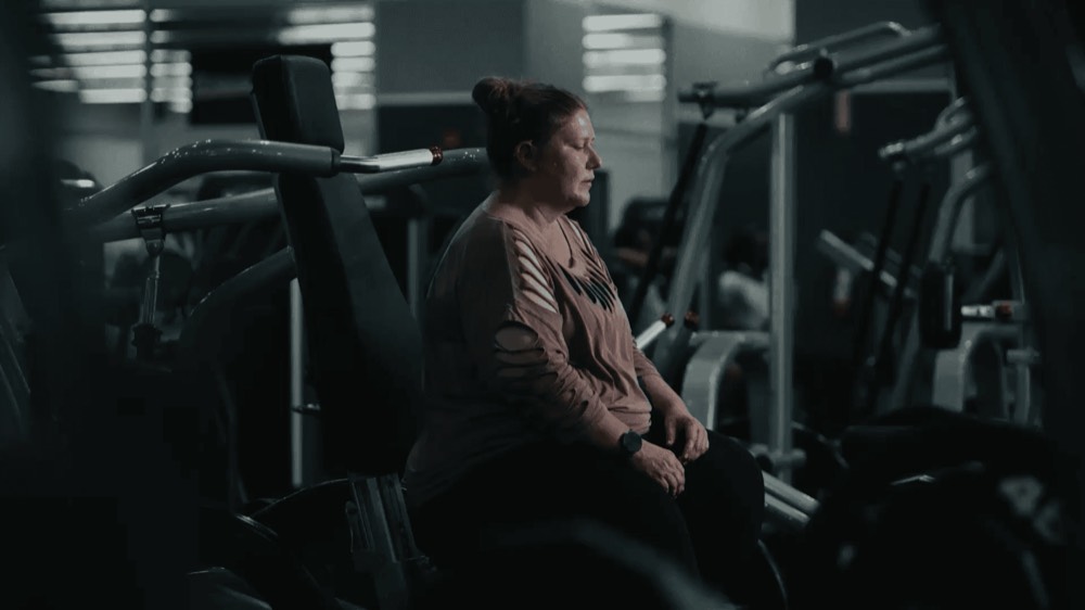 A woman sitting quietly on gym equipment, a still from a Chalant film